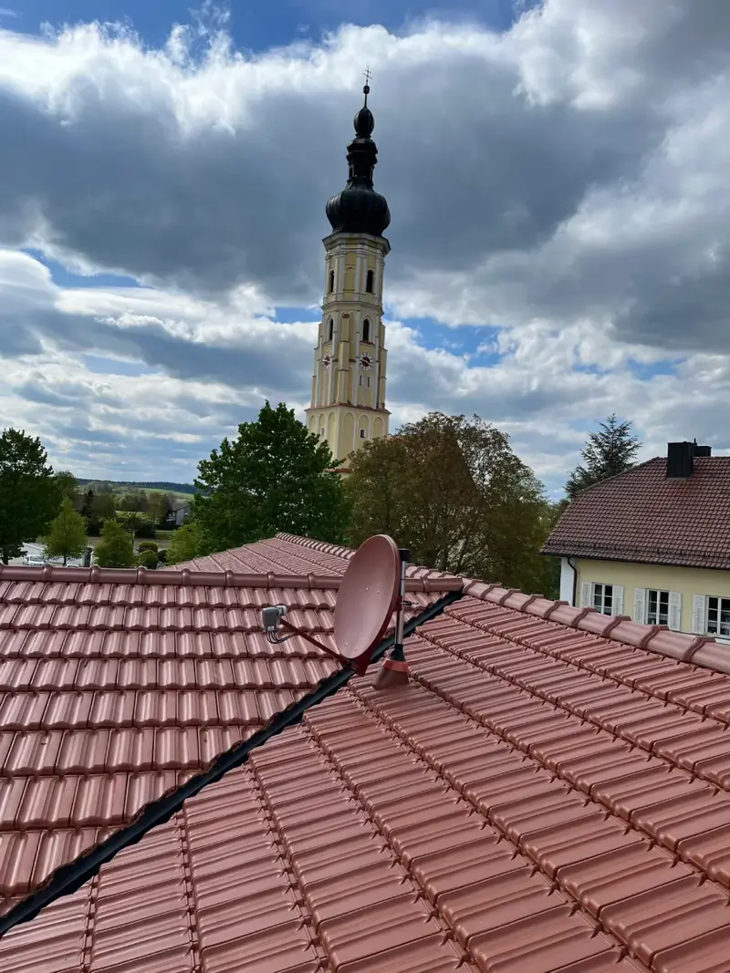 Satellitenschüssel auf einem Ziegeldach vor einem Kirchturm
