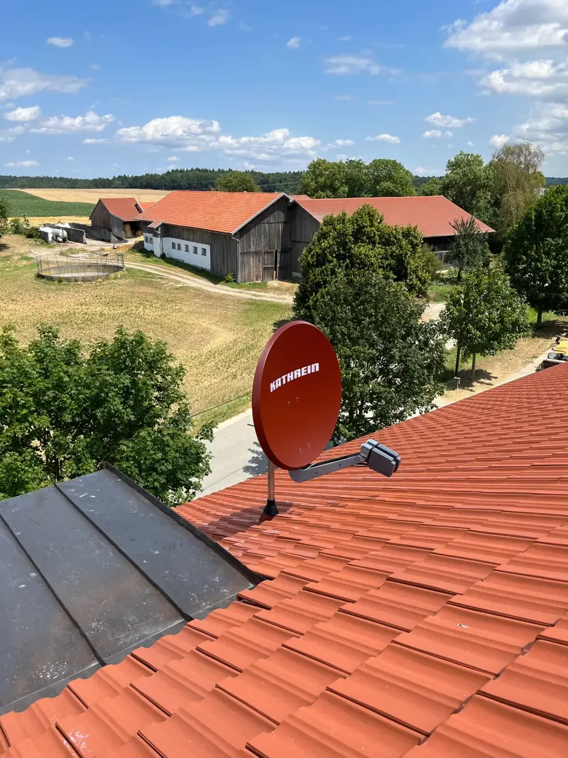 Rote Satellitenschüssel auf einem Ziegeldach mit Blick über das Land